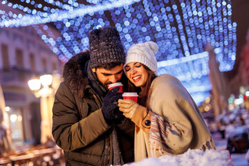 Couple spending Christmas Eve outdoors, drinking hot mulled wine
