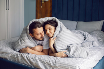 couple in love in white clothes lying under a blanket on the bed in the bedroom in the morning.