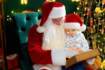 Fototapeta na wymiar Santa Clause reads fairytale to a little boy while sitting near Christmas tree. New Year concept 