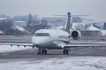 Fototapeta na wymiar business jet plane is driving on the airport taxiway covered with snow in winter.