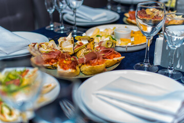 Banquet with snacks. Canapes with bacon and avocado. Various salads on a table with a blue tablecloth. Wine glasses and white plates.