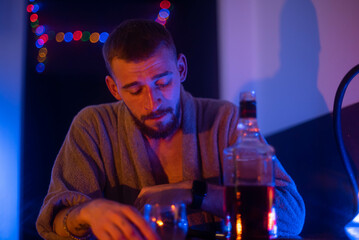 A young man with a beard and a tattoo is sitting in a bar. He has a glass of whiskey in his hands. Meetings with friends. Entertainment for adults.