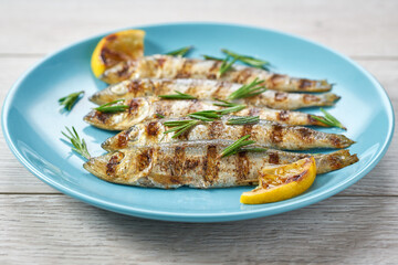 Baked fish with rosemary and lemon on a blue plate, close up.