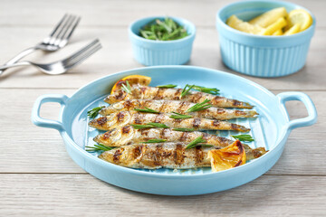 closeup of grilled sardines in a blue plate, on a white wooden table.
