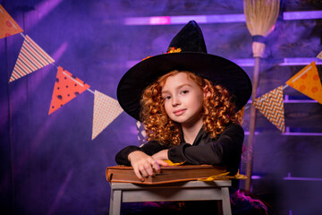 Happy Halloween. Cute cheerful little witch with a magic wand and a book of spells conjures.