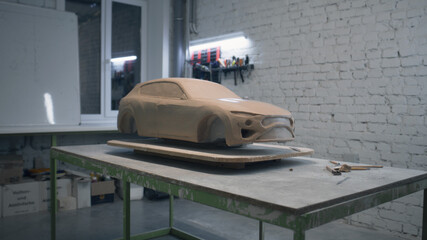 Sculpture of a eco friendly car prototype placed on a wooden table in a workshop with laying sculpting tools. Unfinished sculpture of a prototype model car.
