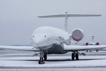 A twin-engine jet plane covered with snow stands at the airport in the parking lot