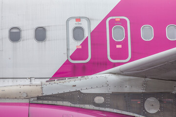 White and pink fuselage of a passenger jet airliner with visible windows and emergency exit doors
