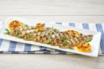 Grilled fish with green rosemary and lemon, white wooden table, with copy space for text.