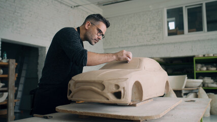 A ceramist works closely on the design details of an unfinished eco friendly electric car prototype...