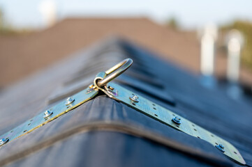 Selective focus on a metal temporary anchor installed on the peak of a roof for fall protection. 