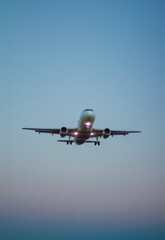 A white and pink jet passenger airliner comes in for landing against a clear sky. Low angle photo from the end of the runway at sunset