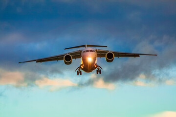 A white and pink jet passenger airliner comes in for landing against a clear sky. Low angle photo from the end of the runway at sunset