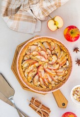 Dessert, round apple pie or shortcrust pastry tart with apple slices and almond petals in a pink shape on a light concrete background. Thanksgiving day concept.
