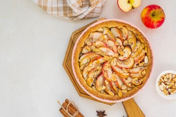Dessert, round apple pie or shortcrust pastry tart with apple slices and almond petals in a pink shape on a light concrete background. Thanksgiving day concept.
