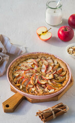 Dessert, round apple pie or shortcrust pastry tart with apple slices and almond petals in a pink shape on a light concrete background. Thanksgiving day concept.