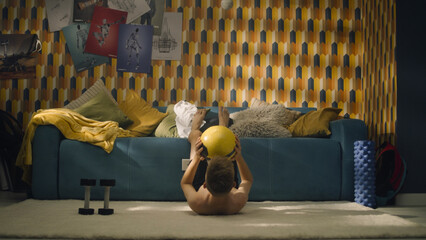 Athletic young boy do upper body biceps workout with a yellow football in his hands. Shirtless...