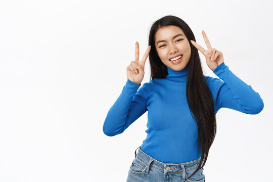 Portrait of beautiful, joyful asian girl dancing and laughing, posing in blue pullover against white background