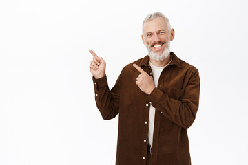 Enthusiastic old man, senior mature person pointing fingers left, smiling and laughing, showing...