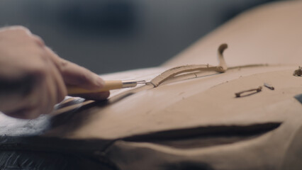 Close-up shot of male automotive designer sculpting car model from plasticine clay with rake....