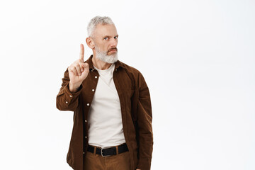Image of senior man, old mature guy shaking finger in disapproval, prohibit smth, standing over...