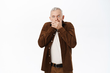 Shocked mature man, old male model looking speechless and stunned at camera, standing over white background