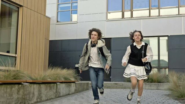 Two students, a girl and a guy, are running around the courtyard of the educational institution. Classmates are in a hurry somewhere. Late for class.