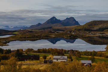 Landscape shot of a mountain range with a grass field at the bottom and a wooden house, Norway