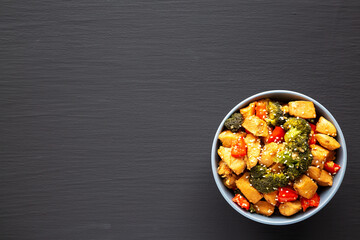 Homemade One-Pan Chicken And Broccoli Stir-Fry in a Bowl on a black background, top view. Flat lay, overhead, from above. Space for text.
