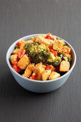 Homemade One-Pan Chicken And Broccoli Stir-Fry in a Bowl on a black background, side view.