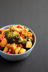 Homemade One-Pan Chicken And Broccoli Stir-Fry in a Bowl on a black background, side view. Space for text.