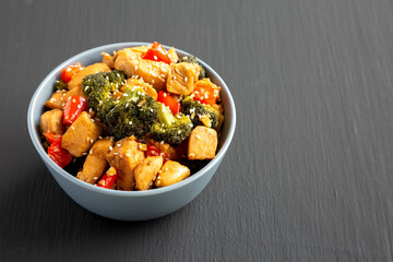 Homemade One-Pan Chicken And Broccoli Stir-Fry in a Bowl on a black background, side view. Space for text.