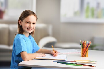 Happy schoolgirl sitting at desk, classroom background