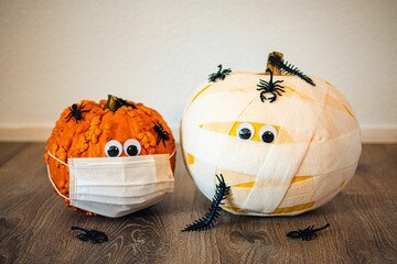 Closeup of two small pumpkins in bandages and in a face mask with worms and spiders on the ground