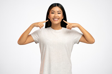 Happy teenager girl in white T-shirt smiling and pointing at herself, being proud of own success
