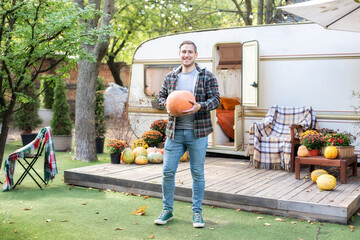 Smiling Man holds big orange pumpkin on porch. Halloween preparation. Happy Farmer holding ripe...