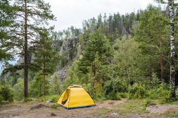 Tourist camping in the mountains, a yellow tent stands in a clearing in the middle of the forest, an open entrance to the tent, a place to sleep in nature, a camping vacation.