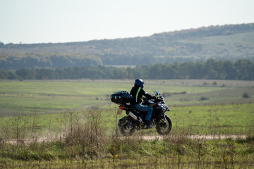 a motor cyclist (biker) riding their sports motorbike along a dusty summer stone track