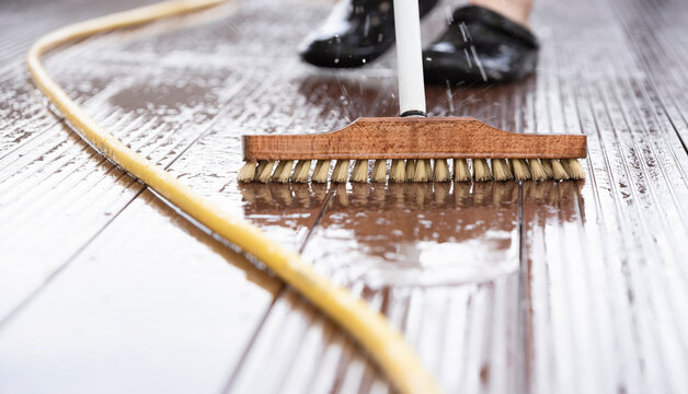 Detail of a scrubber and a water hose during spring cleaning on a wooden terrace