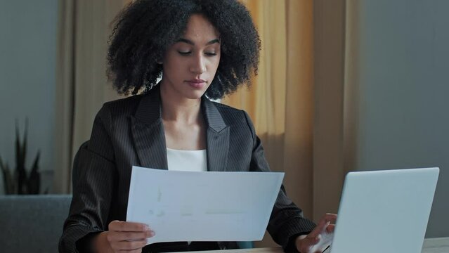 African teacher worker business woman work with graphics documents at home office check documentation enter financial data to laptop processing online information paying bills in computer banking app