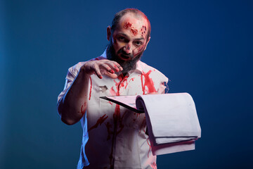 Frightening halloween zombie reading business papers in studio, looking at documents and having...