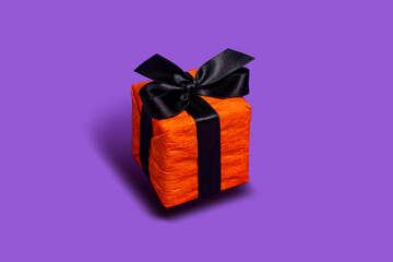 Orange gift box tied with black ribbon isolated on purple background