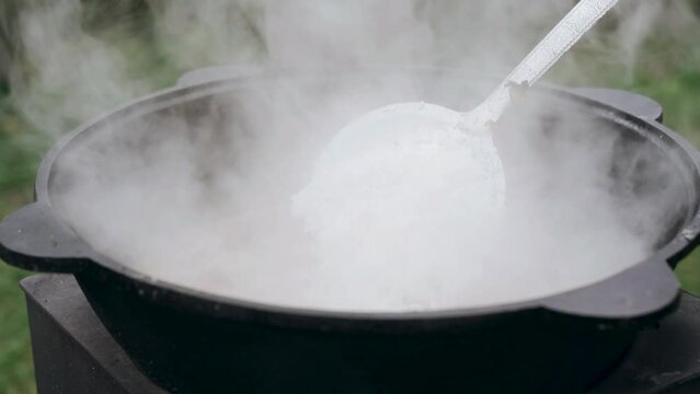The cook pours rice into the cauldron for cooking pilaf in a cast-iron cauldron. Close-up.