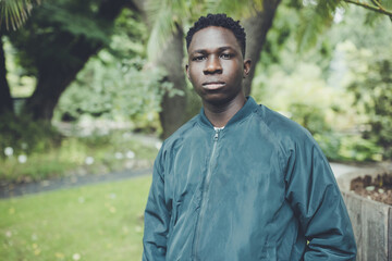 Young African American man in bomber jacket in park. Fall or spring