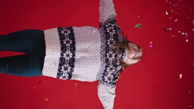 Happy girl in sweater tosses confetti on red background
