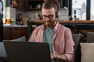 Fototapeta premium A young cheerful man with a sleeve tattoo has an online business meeting, a freelance entrepreneur working from home. 