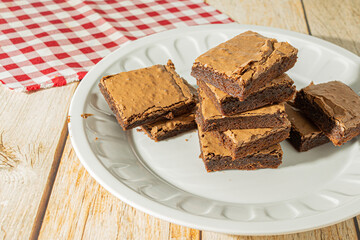 square homemade chocolate brownie over table on a white dish, delicious tasty dessert