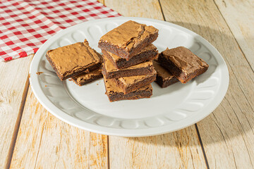 square homemade chocolate brownie over table on a white dish, delicious tasty dessert