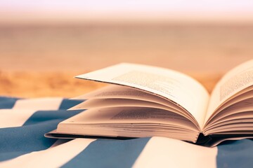 A opened book sitting on the beach sand with a ocean background. Literature and reading.