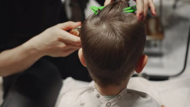 Fashionable hairdresser cuts a child's hair with a clipper in a barbershop. Men's hairstyle and haircut in the salon.